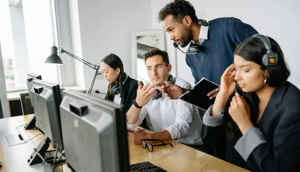 A diverse team of IT professionals collaborating in an office, with headsets on and focused on computer monitors, discussing strategies and providing technical support.